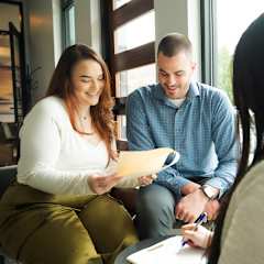 A man and woman are sitting across from each other at a table, looking at a piece of paper.