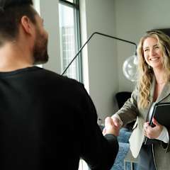 A woman in a business suit shakes hands with a man in a black shirt.