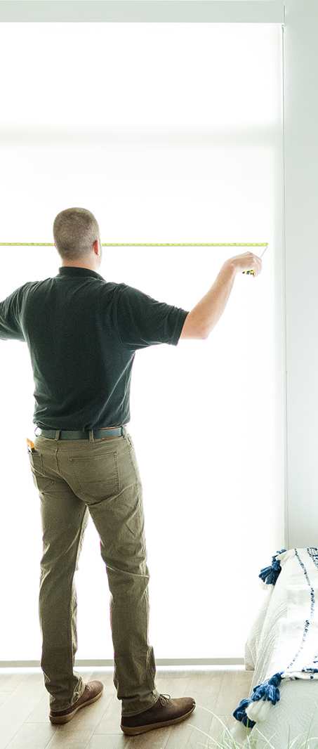 A man is measuring the window with a tape measure.