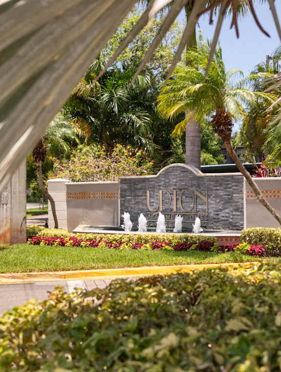 A plaque with fountain in front of a wall with palm trees.