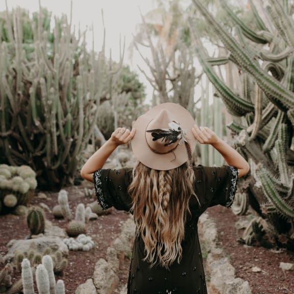 a girl in a hat standing in front of a cactus garden