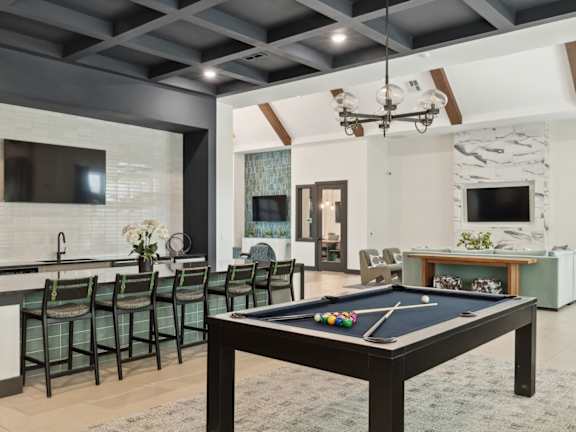A pool table is in the middle of a room with a bar and a television.