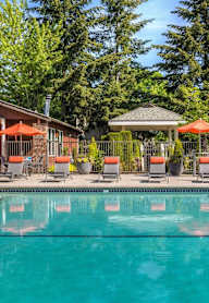 A swimming pool surrounded by a gazebo, chairs, and trees.