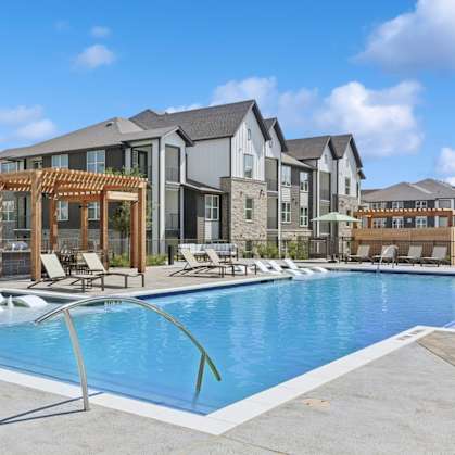 A swimming pool surrounded by lounge chairs and umbrellas in front of apartment buildings.