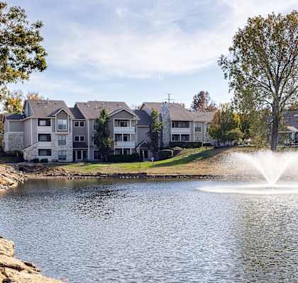 Serene lake view at Three Lakes Apartments, featuring a fountain and apartment buildings surrounded by greenery.