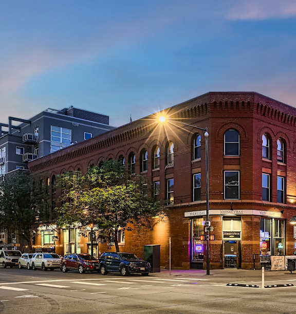 A red brick building with a lit up window on the corner.