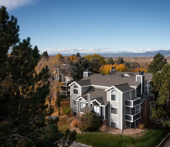 A large house with a grey roof and white walls is surrounded by trees.