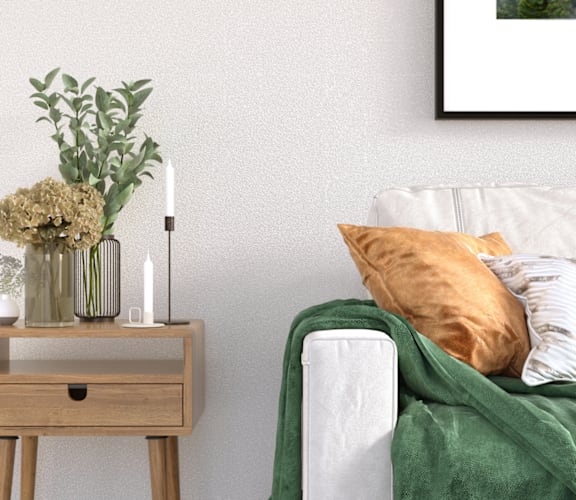 A white couch with a green throw blanket and a wooden table with vases and candles.