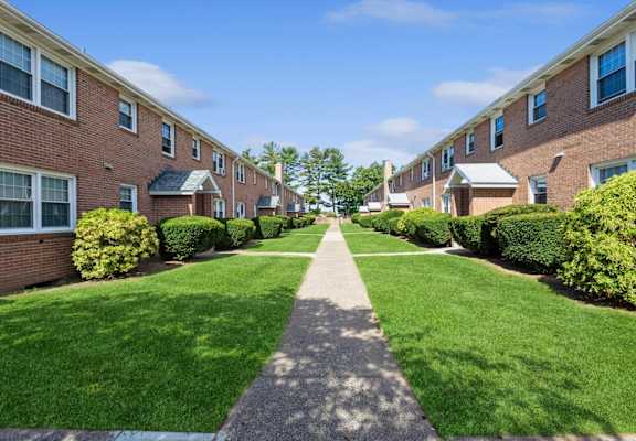 an alley of brick apartment buildings with green grass and a sidewalk