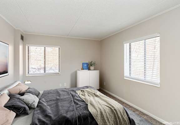A bedroom with a bed, a nightstand, and a window with blinds.