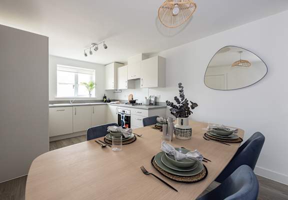 a dining room with a wooden table and a kitchen in the background
