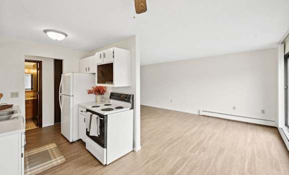 an empty living room with a kitchen with a stove and refrigerator