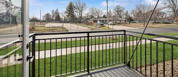A balcony with a black railing overlooks a grassy area and a road.