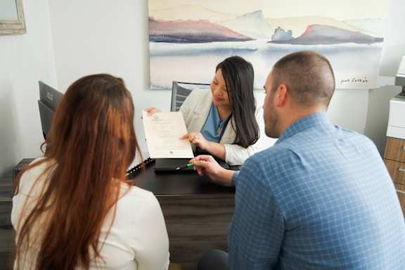 A man and woman are sitting at a desk with a woman holding a document and a laptop open in front of her.
