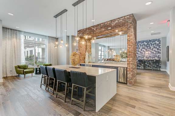 A kitchen with a brick wall and a long island with chairs.