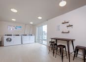 Thumbnail 9 of 9 - Laundry room area of an apartment, fitted with washing machines, seating area, and vinyl flooring.