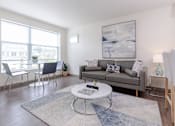 Thumbnail 1 of 9 - Living room area of an apartment, furnished with a sofa, rug, vinyl flooring, and high ceiling