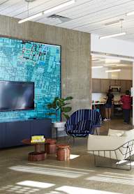 A modern office space with blue chairs and a large screen on the wall.