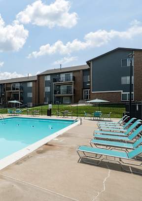 A swimming pool surrounded by sun loungers and apartment buildings.
