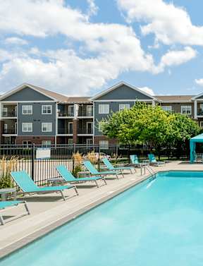 A swimming pool surrounded by sun loungers and apartment buildings.