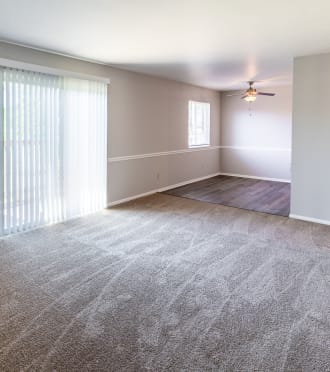 an empty living room with a large window and a ceiling fan