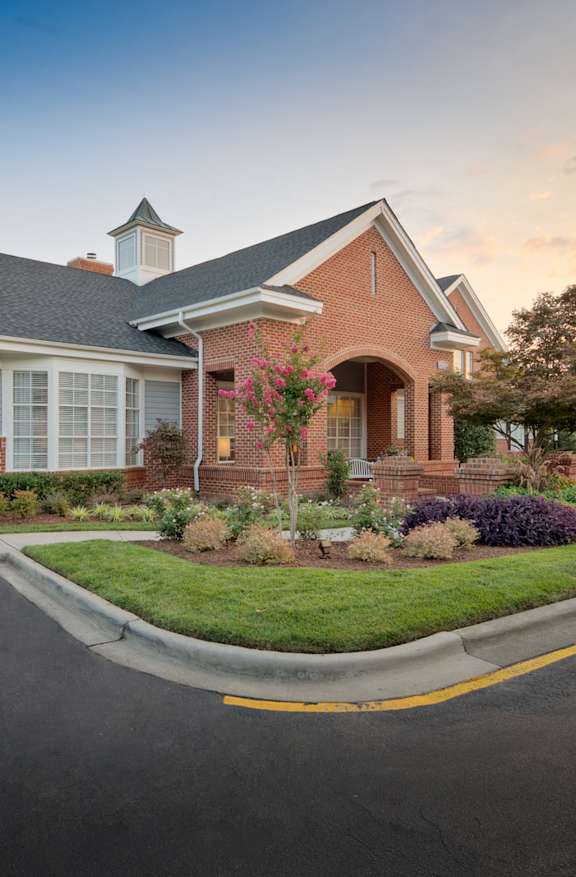 A house with a brick facade and a white roof is surrounded by a well-manicured lawn and a clear sky.