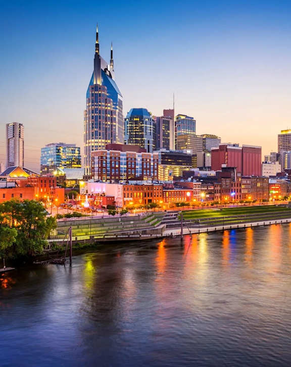 A city skyline at dusk with a river in the foreground.
