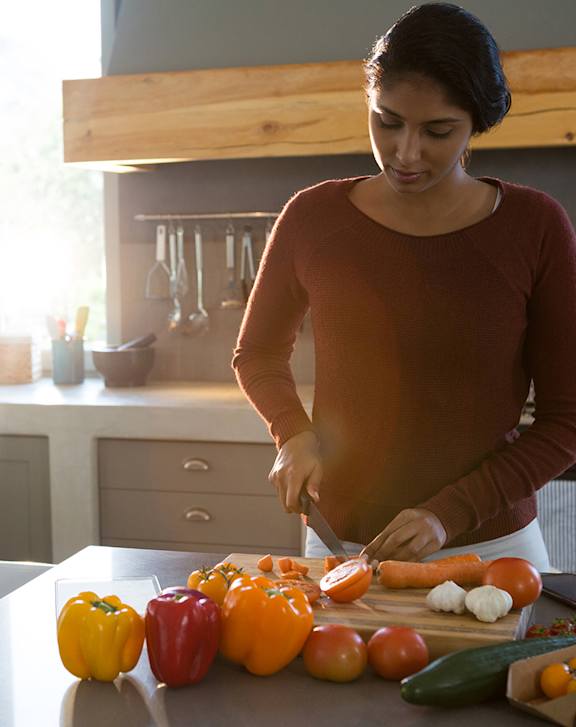 A person in a yellow shirt is holding a bag with vegetables and a phone.