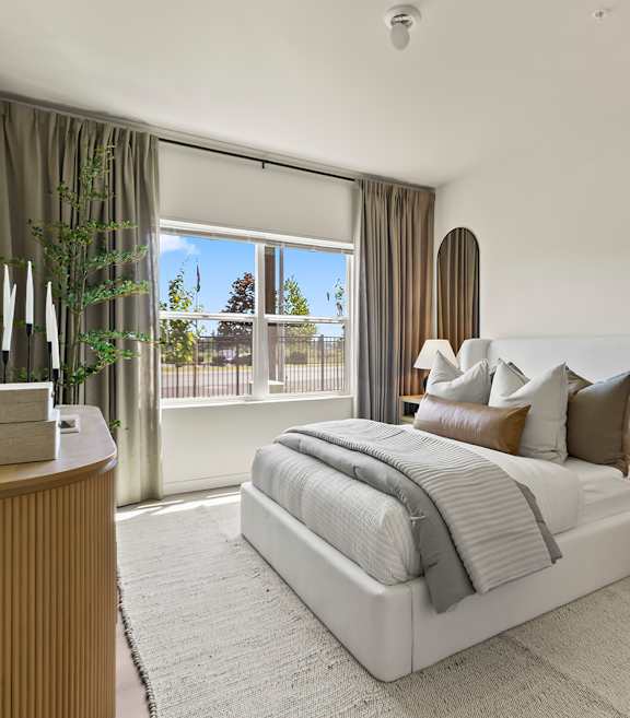 A bedroom with a large bed, a wooden nightstand, and a large window with curtains.