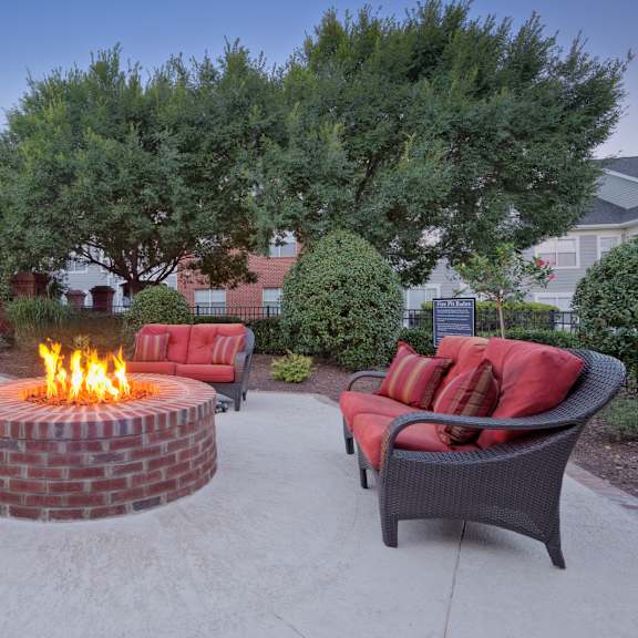 A fire pit in the middle of a patio surrounded by chairs and plants.