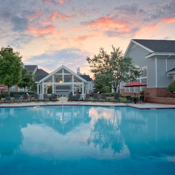 A large swimming pool in front of a house with a sunset in the background.