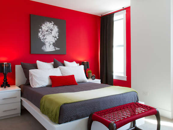 A bedroom with a bed, nightstands, and a red chair.