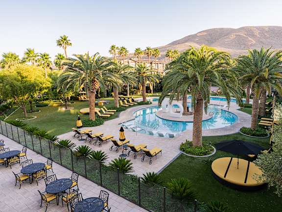 A pool surrounded by palm trees and lounge chairs.