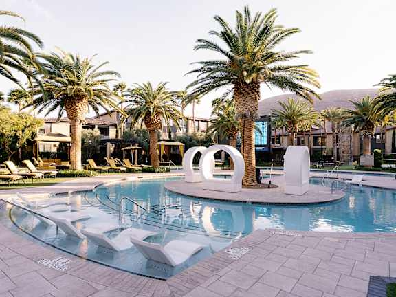 A pool surrounded by palm trees and a white sculpture.