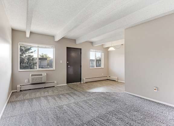 A spacious room with a grey carpet and a window overlooking a tree. at Park at Fitzsimons Apartments, Aurora, MO, 80011