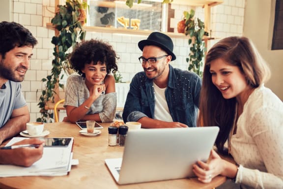 a group of people sitting around a table looking at a laptop