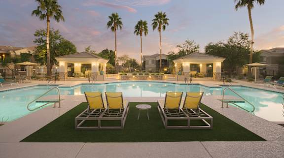 A pool with two chairs and a table in the foreground with palm trees in the background.