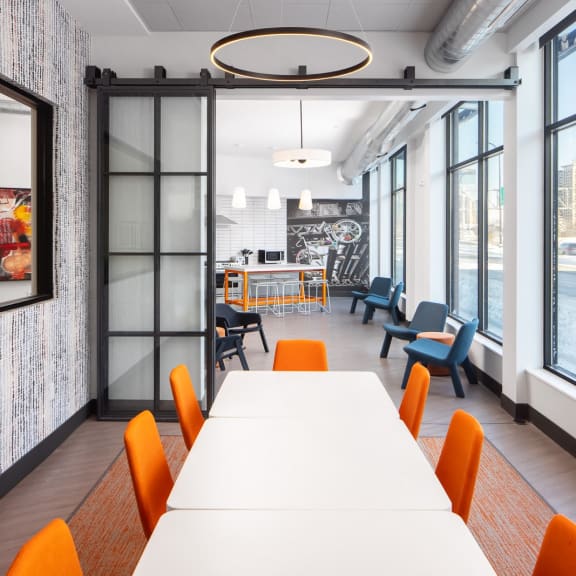 a long table with orange chairs in a room with large windows