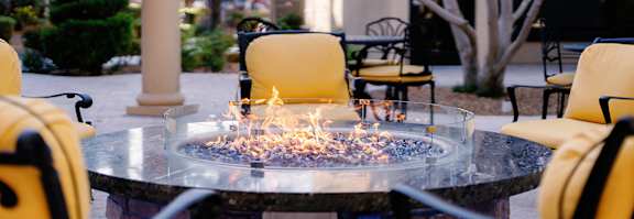 A fire pit in the middle of a patio surrounded by yellow chairs.