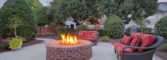 A fire pit in the middle of a patio surrounded by chairs and plants.