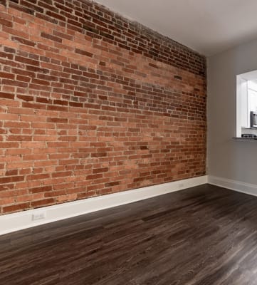 an empty living room with a brick wall and hardwood floors at Lockerbie Court on Mass Ave Apartments, Indianapolis, Indiana