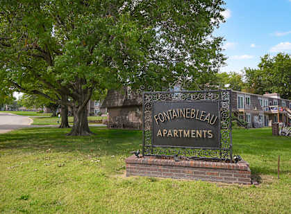 A sign that says "Fontainebleau Apartments" in front of a grassy area.