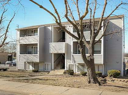 A tree in front of a two-story apartment building.