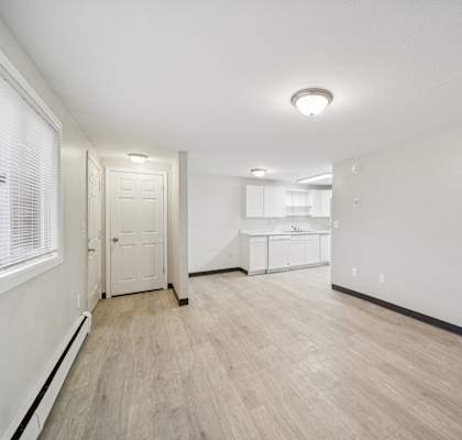 A white room with a wooden floor and a window with blinds.