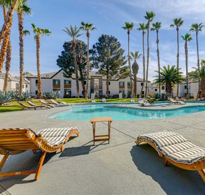 A pool surrounded by palm trees and lounge chairs.
