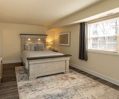 A bedroom with a bed, nightstand, and a rug. at Liberty Gardens Apartments, Baltimore