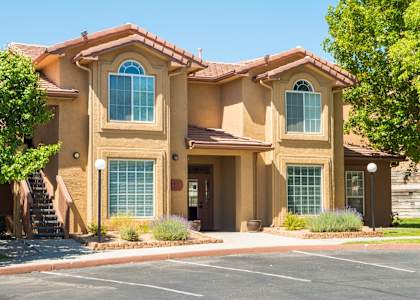 A beige house with a brown roof and a parking lot in front at West Park Apartments, Albuquerque, NM