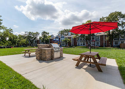 A picnic table with a red umbrella is in the middle of a concrete area.