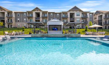 a large swimming pool with lounge chairs and umbrellas in front of an apartment building at The Prairie Luxury Apartments, Dardenne Prairie, MO