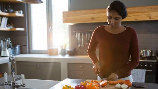 A woman is cutting vegetables in a kitchen.
